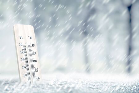 Wooden thermometer with the low temperature at winter with snowfall background