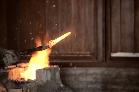 Blacksmith forging the molten metal with a hammer to make keris in the blacksmith's workshop
