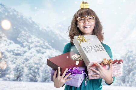 Asian woman holding gift box with Boxing Day Sale text with snowy hill background