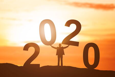 Silhouette of businessman put 2020 on the top of the hill with a sunset sky background. Happy New Year 2020の写真素材
