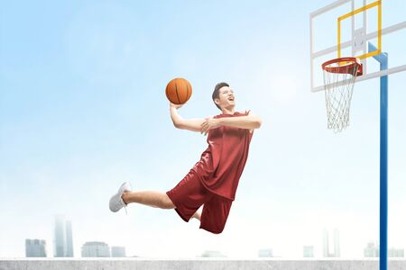 Asian basketball player man jumps in the air with the ball trying to score on the basketball court