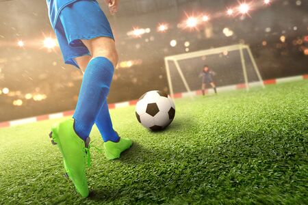 Rear view of football player man kicking the ball on the football field at the stadiumの写真素材