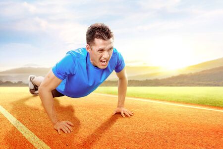 Asian man doing workout push up on the running track with a blue sky background