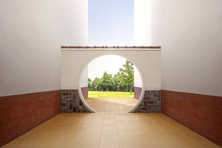 Chinese round gate with view of green grass and trees over blue sky backgroundの写真素材