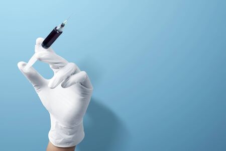 Doctor man in protective gloves holding a syringe with blue background