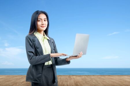 Asian businesswoman standing while using a laptop at outdoorの写真素材