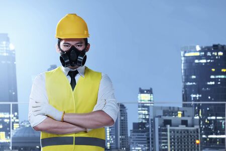 Asian worker man with a protective mask and yellow helmet standing with city background. Labor day...