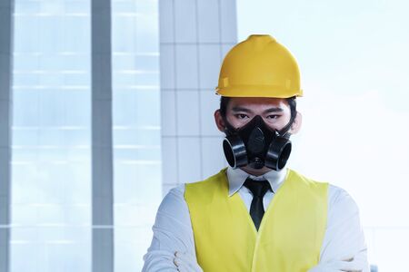 Asian worker man with a protective mask and yellow helmet standing with building background. Labor day conceptの写真素材
