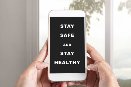 Hands holding a mobile phone with a message for Stay safe and stay healthy on the screen. Prevent...