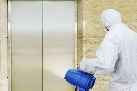 Man in a white protective suit spraying disinfectant in the office building. Prevent the spread flu disease Coronavirusの写真素材
