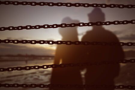 Chain fence with a couple standing on the beach at sunset. World Refugee Day Concept 