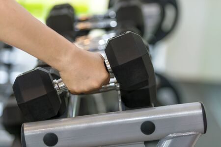 Man hand taking dumbbell on a rack in the gym