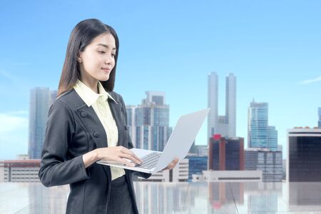 Asian businesswoman standing and reading news on her laptop with cityscape backgroundの写真素材