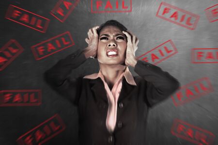 Asian businesswoman feeling depressed with the text of fail on the wall backgroundの写真素材