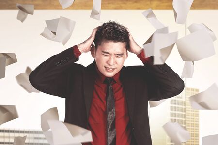 Asian businessman feeling depressed with flying work papers on the workplaceの写真素材