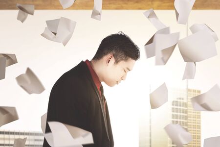 Asian businessman feeling depressed with flying work papers on the workplaceの写真素材