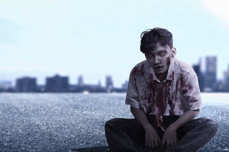 Scary zombie with blood and wound on his body sitting on the cityの写真素材