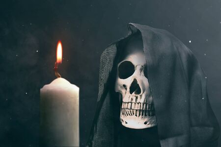 Human skull with a black cloak and burning candle on dark background. Halloween conceptの写真素材