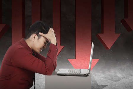Asian businessman feeling depressed looking global economic impact report on the laptop because...
