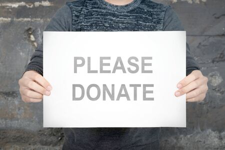 Man holding a white paper with please donate text with wall backgroundの写真素材