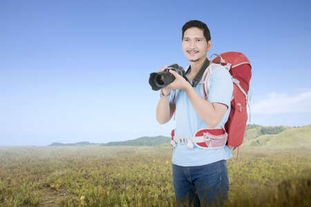 Asian man with a backpack holding the camera on the meadow field. World Photography Dayの写真素材