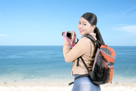 Asian woman with a backpack holding the camera on the beach. World Photography Dayの写真素材