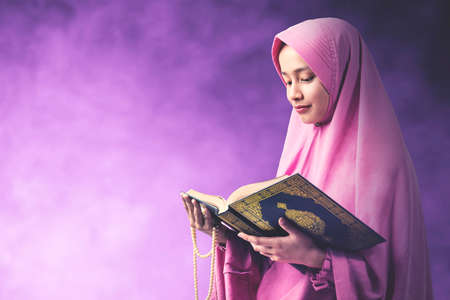 Asian Muslim woman in a veil holding prayer beads and reading the Quran with a colored background. Islamic New Yearの写真素材