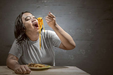 Asian man eating spaghetti at home. Junk food concept