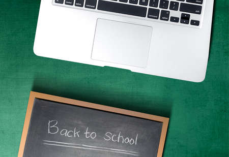 Small blackboard with the text of back to school and laptop on green background