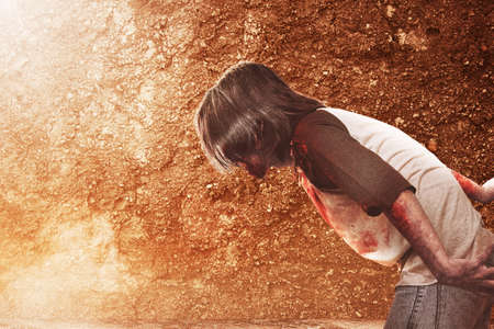 Scary zombie with blood and wound on his body walking on the floor with a dirty wall background