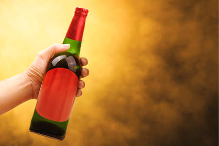 Hand holding beer bottle with a yellow background. Beer for celebrating Oktoberfestの写真素材