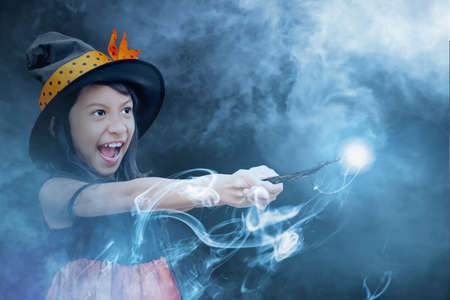 Asian witch little girl using the wand with a magic shine with mystical fire with smog backgroundの写真素材
