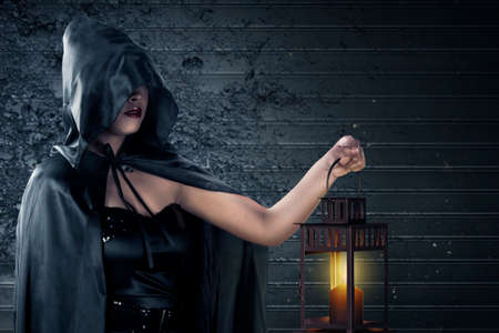 Asian witch woman with black cloak holding lantern standing with grunge wall background