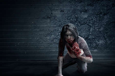 Scary zombie with blood and wound on his body eat the raw meat with grunge wall backgroundの写真素材