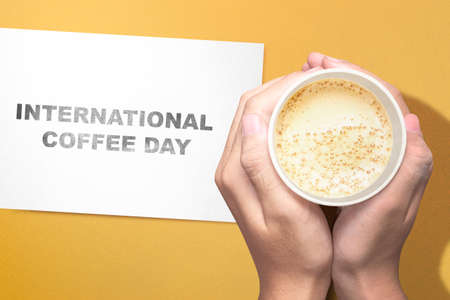 Human hands holding a cup of coffee with a colored background. International Coffee Dayの写真素材
