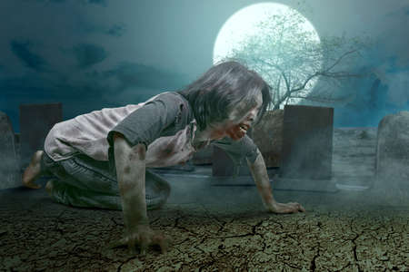 Scary zombie with blood and wound on his body crawling on the graveyard