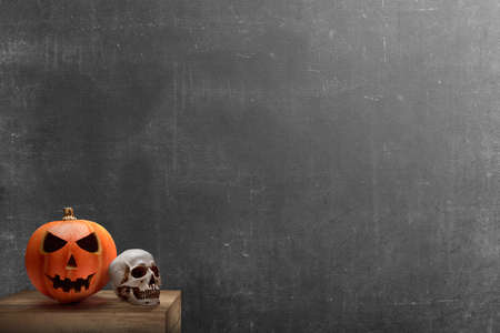 Jack-o-Lantern and human skull on the table with black wall backgroundの写真素材