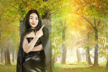 Asian witch woman with a cloak standing and showing with an empty space with a forest background. Empty space for copy spaceの写真素材