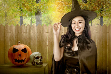 Asian witch woman with a hat standing with a wooden fence on forest background