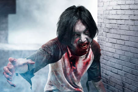 Scary zombie with blood and wound on his body walking in the abandoned building