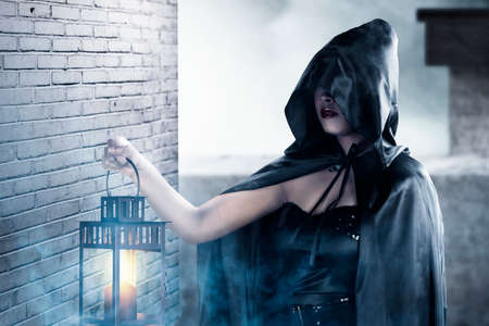 Asian witch woman with a cloak holding a lantern standing in the abandoned building