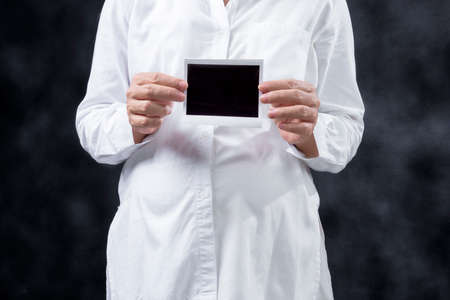 Pregnant woman holding ultrasound pregnancy test result with black backgroundの写真素材
