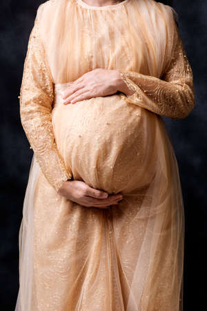 Pregnant woman in dress holds hands on belly with black backgroundの写真素材