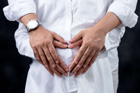 Pregnant couple touching belly and showing heart symbol with hand with black background