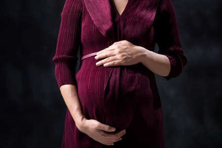 Pregnant woman in dress holds hands on the belly with black backgroundの写真素材