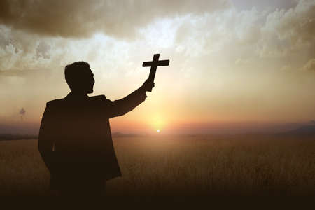 Silhouette of a businessman holding Christian cross with a sunset sky background