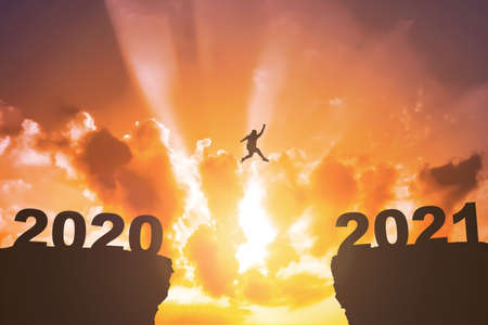 Silhouette of the fat man jumping from hill 2020 to hill 2021 with sunset background. Happy New Year 2021の写真素材