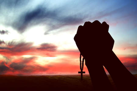 Silhouette of human hands raised while praying with prayer beads to god with a sunrise sky backgroundの写真素材