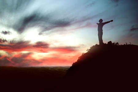 Silhouette of businessman raised hands and praying to god with a sunrise sky background