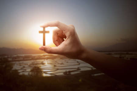 Human hand holding Christian cross with a sunset sky backgroundの写真素材